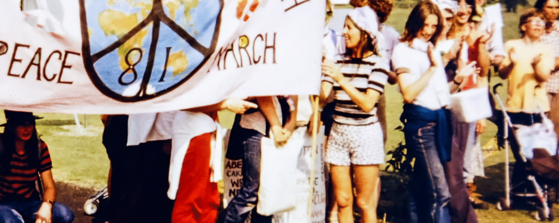 Grupo de personas participando en una manifestación con una pancarta que muestra un símbolo de paz y el mensaje sobre la marcha por la vida y la paz.