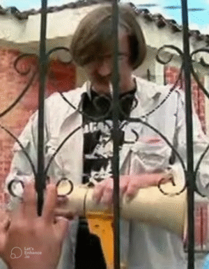 Hombre joven detrás de una reja metálica manipulando un objeto cilíndrico mientras otra persona le pasa algo con la mano.