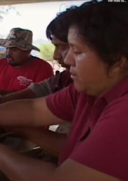 Tres personas sentadas trabajando juntas en una mesa durante una actividad comunitaria.
