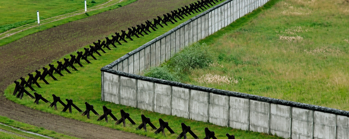 Muro fronterizo de hormigón rodeado de campos verdes en D'un mur l'autre, de Patric Jean.