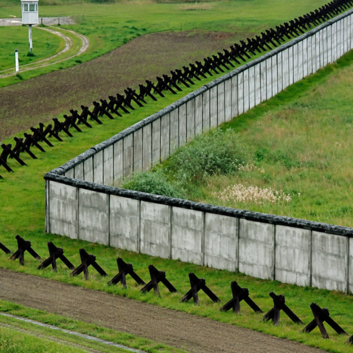 Muro fronterizo de hormigón rodeado de campos verdes en D'un mur l'autre, de Patric Jean.