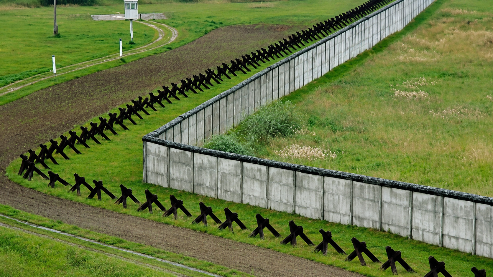 Muro fronterizo de hormigón rodeado de campos verdes en D'un mur l'autre, de Patric Jean.