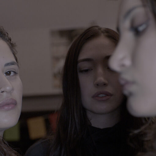 Tres mujeres en un primer plano. Una mira directamente a la cámara mientras las otras dos están de perfil o con la mirada baja.