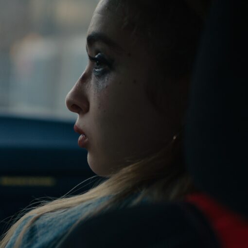 Primer plano de perfil de una joven con maquillaje corrido, mirando por la ventana de un coche.