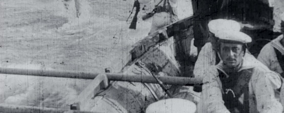 Imagen en blanco y negro de marineros en un barco, con hombres caminando en el agua al fondo.