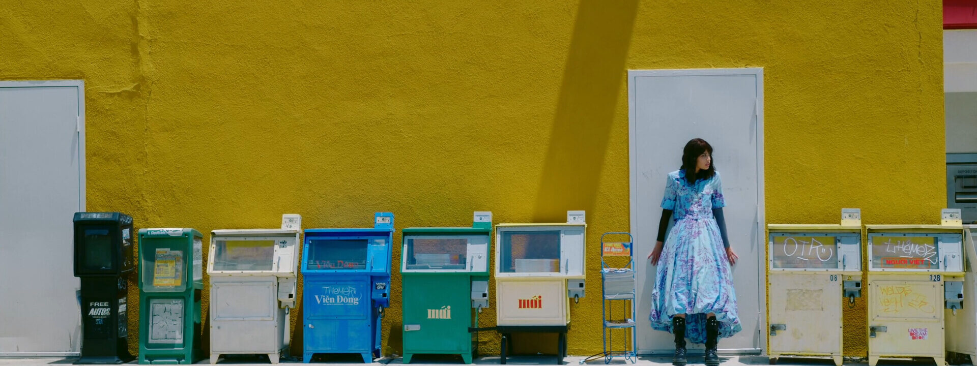 Fotograma del largometraje Ansiedad donde aparece la protagonista apoyada a una puerta y a su lado surtidores de periodicos.