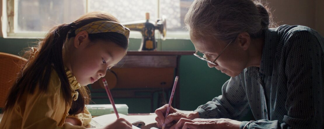 Fotograma del largometraje La respuesta para siempre, donde una anciana y una niña pequeña escriben sobre una mesa.