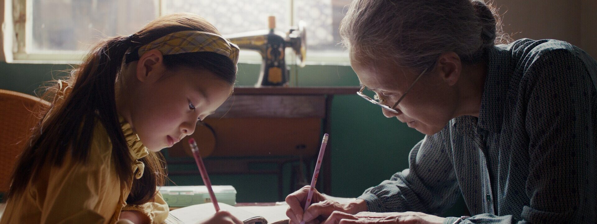 Fotograma del largometraje La respuesta para siempre, donde una anciana y una niña pequeña escriben sobre una mesa.