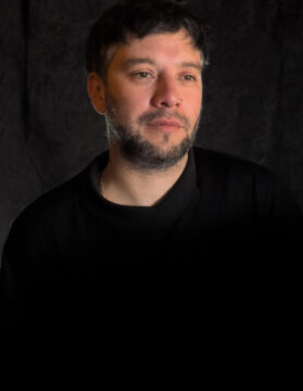 Fotografía 3/4 del director de la Película Cuatro estrellas, Pablo Stigliani con un jersey negro y fondo oscuro.