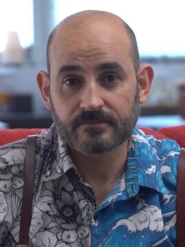 Fotografía de Jesús Pamplona Codirector del documental. Viste camisa estampada con olas de color azul y blanco en una mitad de la camisa y en la otra flores en blanco y negro. Tiene barba y bigote perfilada y no tiene pelo en la parte superior de la cabeza.