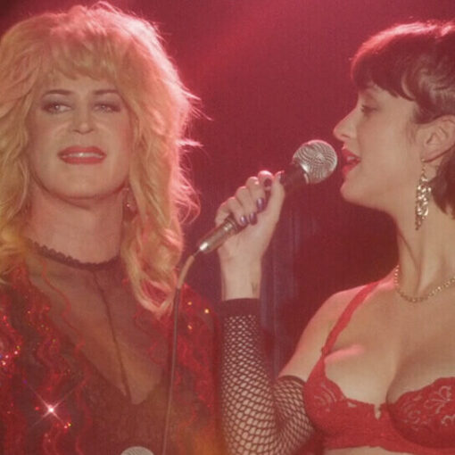Fotograma de la película Cuatro Estrellas donde aparecen una mujer trans al lado de otra en un escenario, mientras sostienen dos micrófonos y llevan a cabo una actuación.