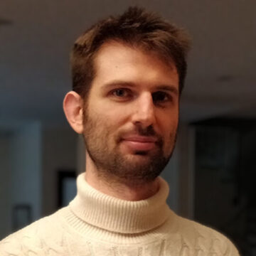 Fotografía retrato del directo Alessandro Ricondo, pelo corto y castano, barba corta y jersey de cuello alto blanco.