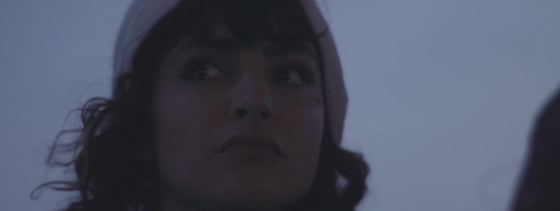 Fotograma de El Gato. Una mujer joven de pelo negro y con un pañuelo en la cabeza aparece en primer plano, con su mirada fija en algo que tiene delante.