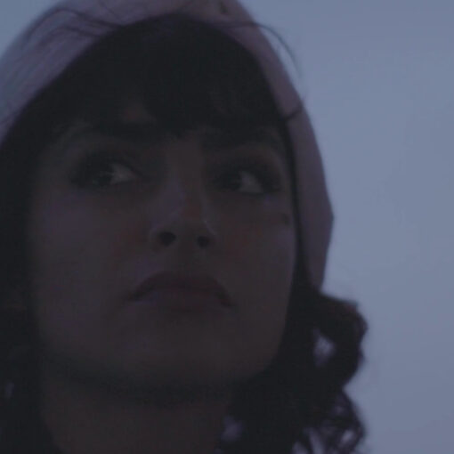 Fotograma de El Gato. Una mujer joven de pelo negro y con un pañuelo en la cabeza aparece en primer plano, con su mirada fija en algo que tiene delante.