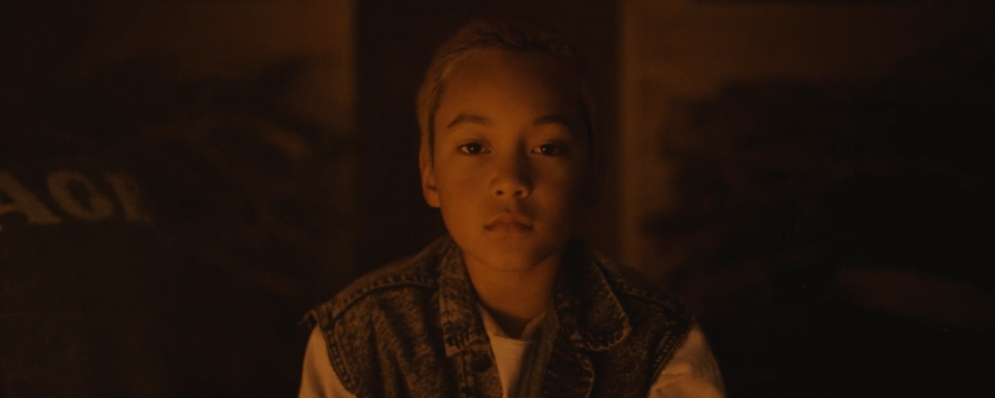 Fotograma de As en el que aparece un niño mirando a cámara con una luz tenue.