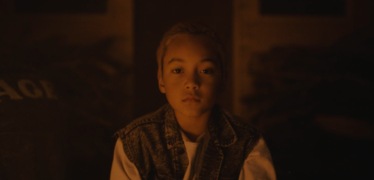 Fotograma de As en el que aparece un niño mirando a cámara con una luz tenue.