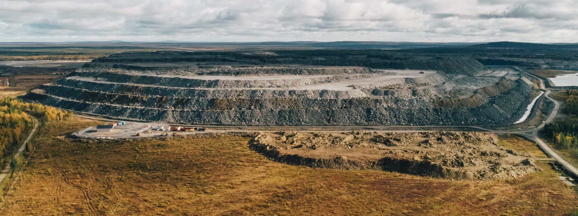 Vista panorámica de una mina a cielo abierto rodeada de paisaje natural bajo un cielo nublado.