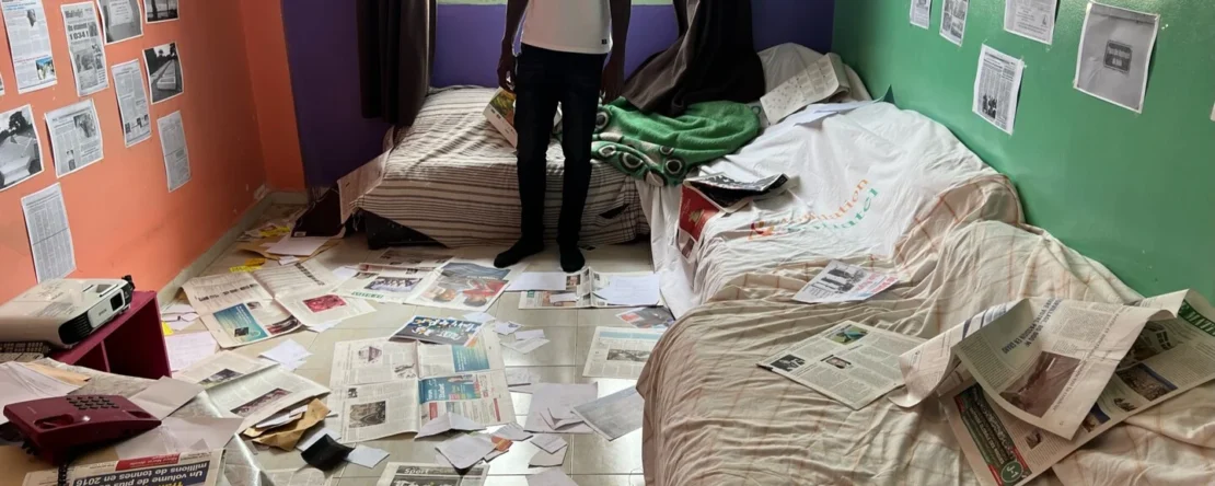 Fotograma de 2002 Batalla contra el olvido en el que aparece un hombre de pie en una habitación desordenada con el suelo y las paredes llenas de páginas de periódicos.