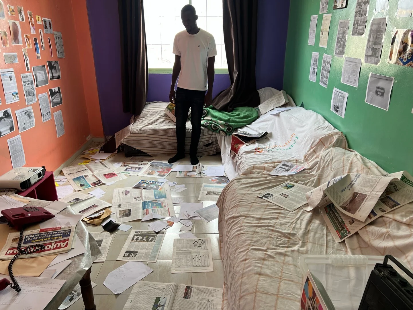 Fotograma de 2002 Batalla contra el olvido en el que aparece un hombre de pie en una habitación desordenada con el suelo y las paredes llenas de páginas de periódicos.