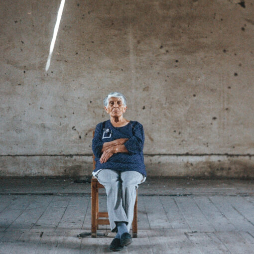 Fotograma de Ecos de luz en el que aparece un hombre canoso sentado en una silla de madera, con los brazos cruzados.