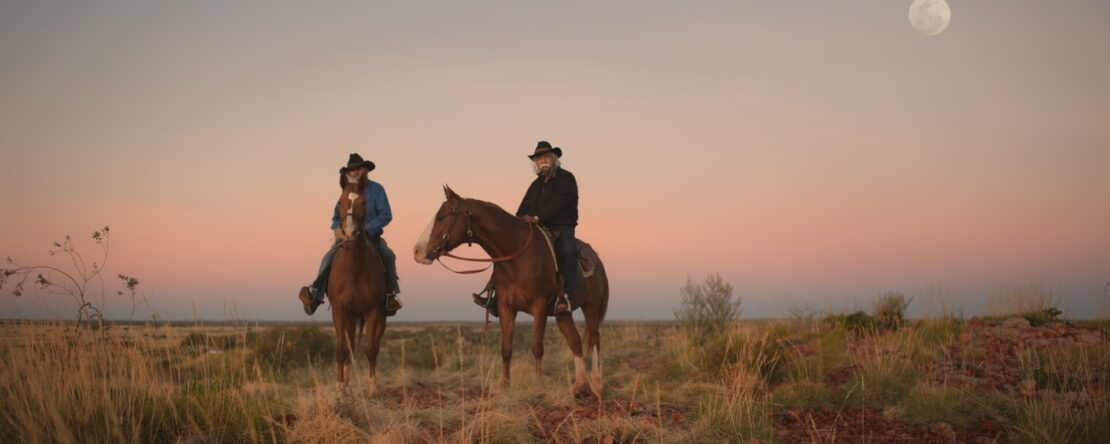 Fotograma de Yurlu | País dos hombres vestidos de vaqueros sobre caballos en un paisaje desértico. En el cielo, está la luna.