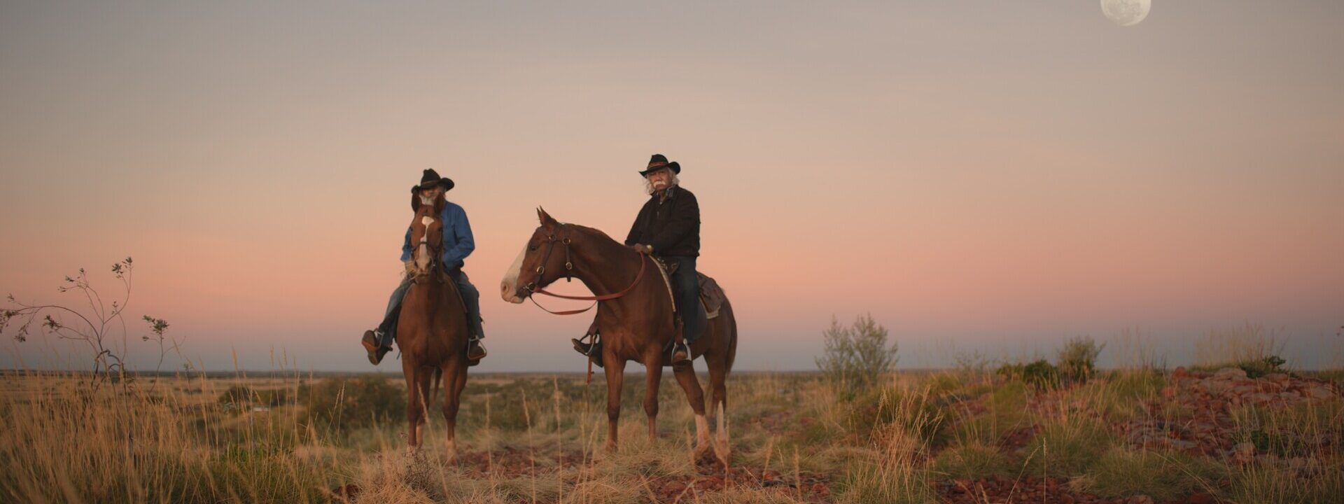 Fotograma de Yurlu | País dos hombres vestidos de vaqueros sobre caballos en un paisaje desértico. En el cielo, está la luna.