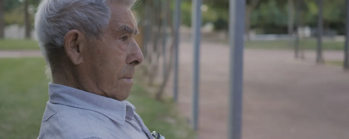 Fotograma de Guerrillero en el que aparece un hombre canoso sentado en un parque y mirando hacia la derecha.