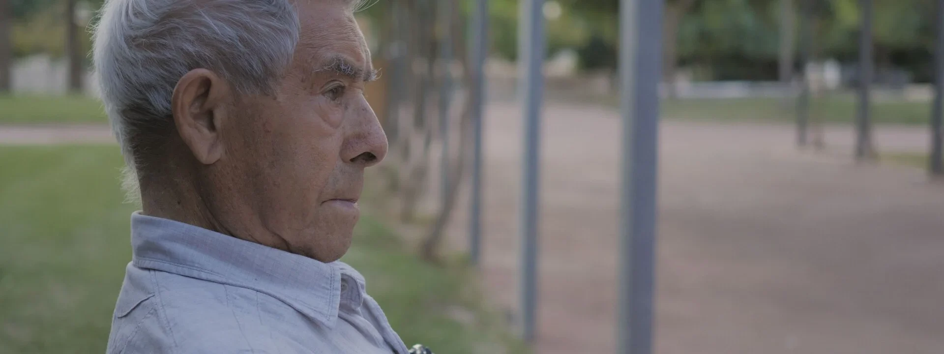 Fotograma de Guerrillero en el que aparece un hombre canoso sentado en un parque y mirando hacia la derecha.